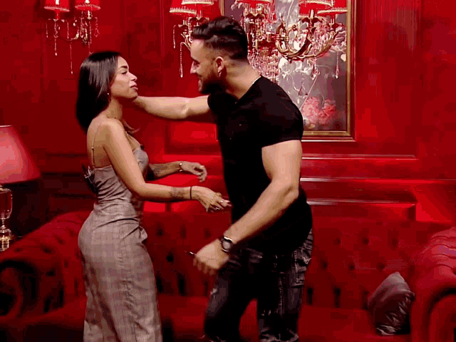 a man and a woman are standing next to each other in front of a red wall