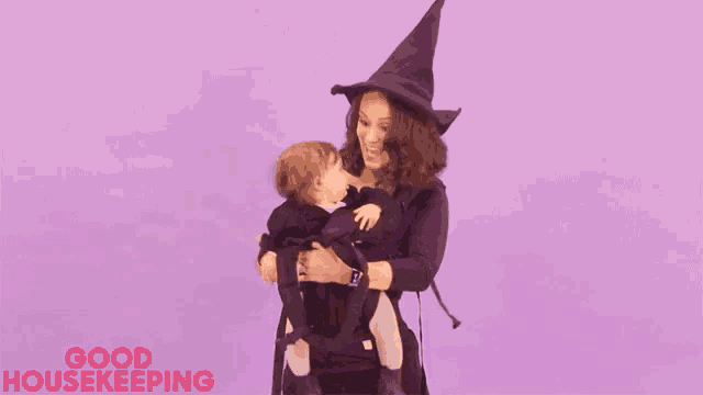 a woman is wearing a witch hat and holding a baby in a carrier .