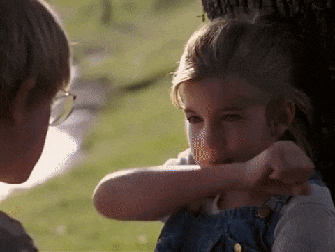 a boy and a girl are sitting under a tree . the girl is covering her face with her hand .