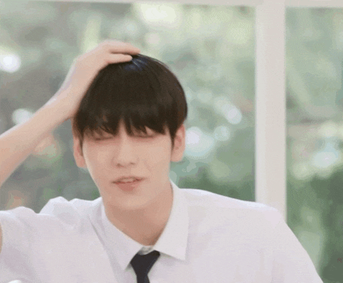 a young man in a white shirt and tie is rubbing his head