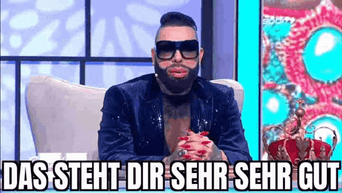 a man with a beard and sunglasses is sitting in a chair and making a funny face .