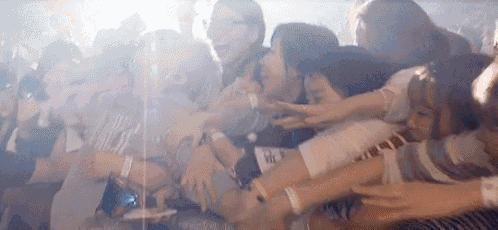 a group of people are standing in a crowd at a concert and hugging each other .