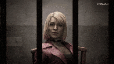 a woman in a red jacket sits in a chair behind bars with konami written on the bottom