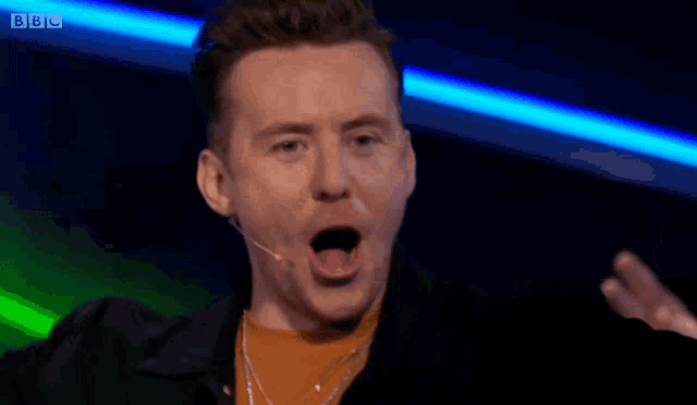 a man speaking into a microphone with the bbc logo in the corner