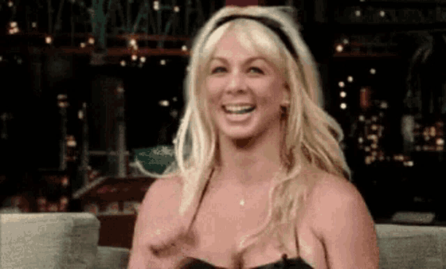 a blonde woman is sitting on a couch smiling .