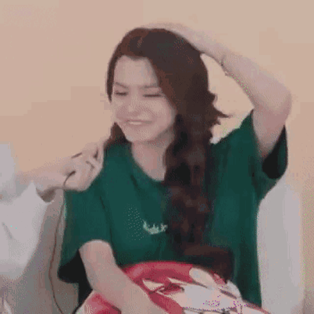 a woman in a green shirt is smiling while holding her hair in a braid .