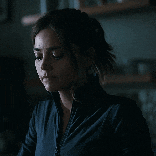 a woman in a dark room with a blue jacket on