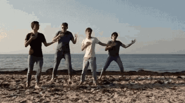 a group of young men are dancing on a beach near the ocean