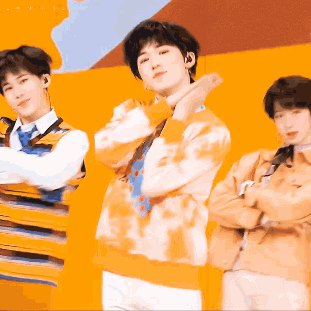 three young men are standing next to each other with their arms crossed in front of an orange background