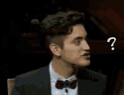 a man in a suit and bow tie is making a funny face with a question mark on his face .
