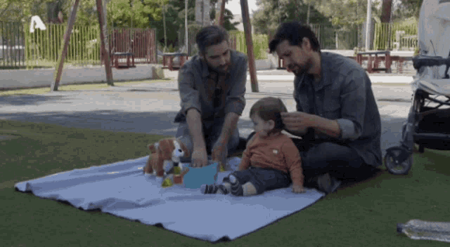 two men playing with a baby on a blanket