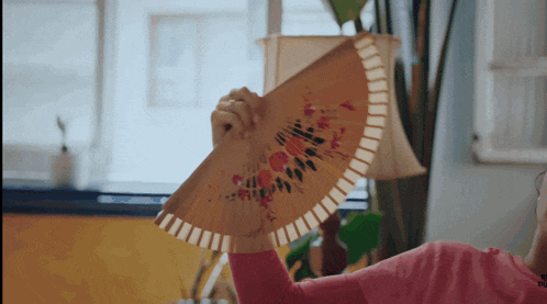 a girl in a pink shirt is holding a fan in her hand