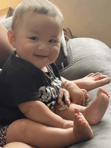 a baby is sitting on a couch wearing a black shirt that says skulls