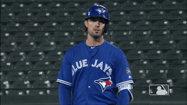 a man wearing a blue jays jersey stands in the outfield