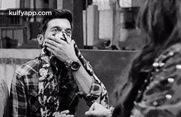 a man is covering his mouth with his hand while talking to a woman in a black and white photo .