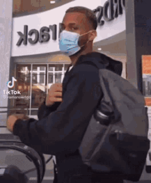 a man wearing a mask and carrying a backpack is walking on an escalator .