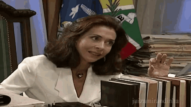 a woman sitting at a desk with a stack of books and a flag with the letter a on it