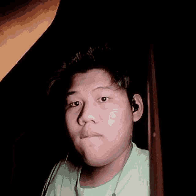 a young man wearing ear buds and a green shirt is making a funny face