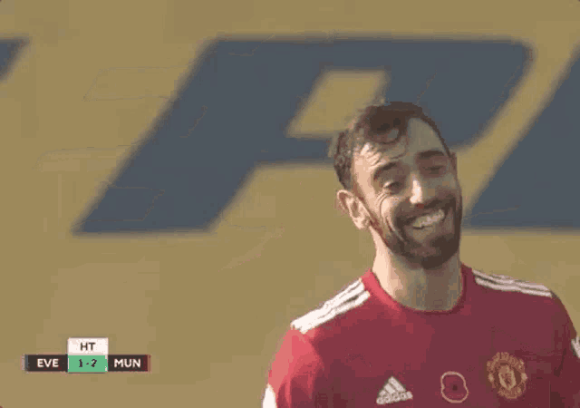 a man with a beard is wearing a red jersey and smiling while playing soccer .