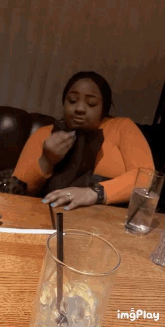 a woman is sitting at a table with a glass of water and a straw in front of her