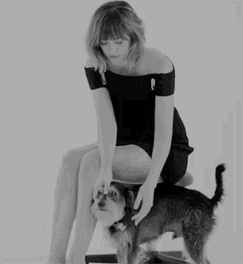 a woman in a black dress sits on a chair with a dog on her lap