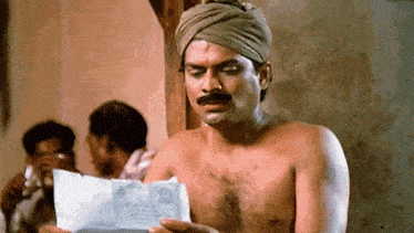 a shirtless man with a turban on his head is holding a piece of paper .