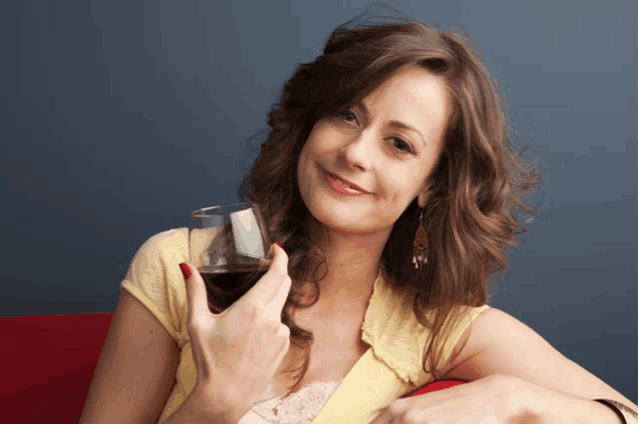 a woman in a yellow shirt holds a glass of red wine