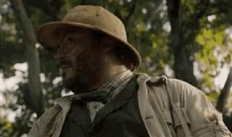 a man with a beard wearing a hat and tie is standing in a forest .