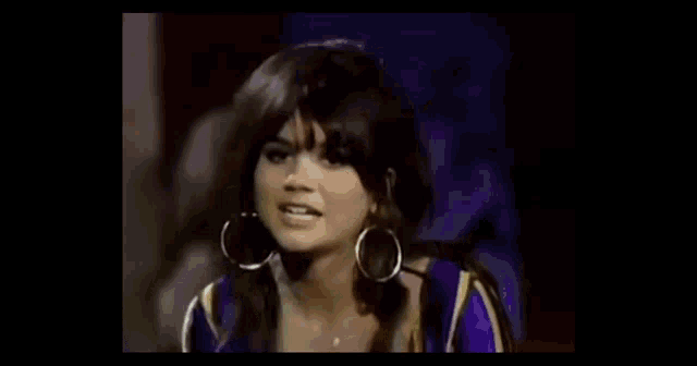 a woman wearing hoop earrings and a purple dress is talking to someone .