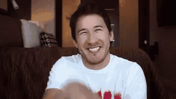 a man in a white shirt is sitting on a couch smiling .