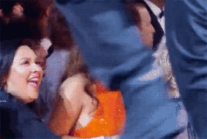 a woman in an orange dress is laughing while sitting in a crowd .