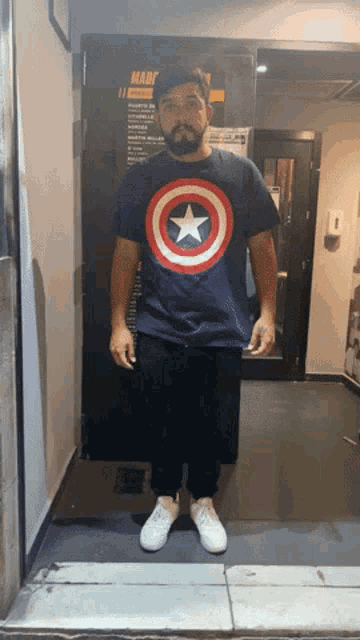 a man in a captain america shirt stands in front of a door