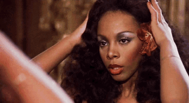 a woman adjusts her hair while looking at herself in the mirror