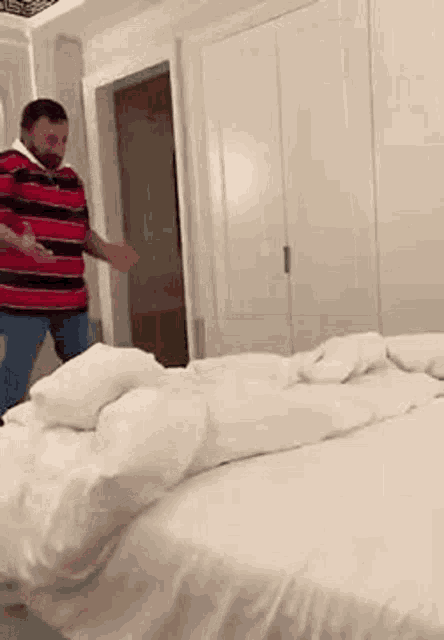 a man in a red and blue striped shirt is standing next to a bed in a bedroom .