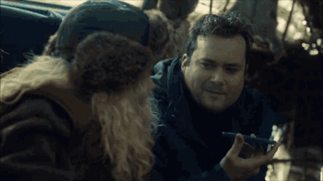 a man in a fur hat talks to another man while holding a cell phone