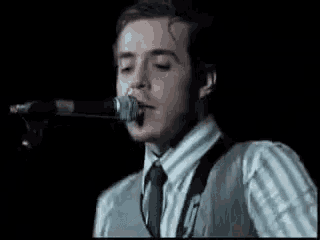 a man is singing into a microphone while wearing a striped shirt and tie .