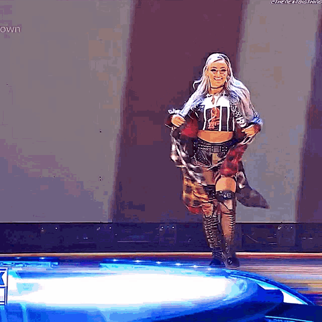 a woman in a crop top and knee high boots is walking on a stage .