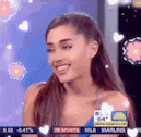 ariana grande is smiling and looking at the camera while sitting on a stage .