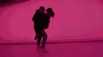 a man is holding a woman in his arms while dancing in front of a pink wall .