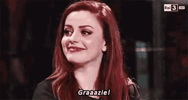 a woman with red hair is smiling and saying graaazie .