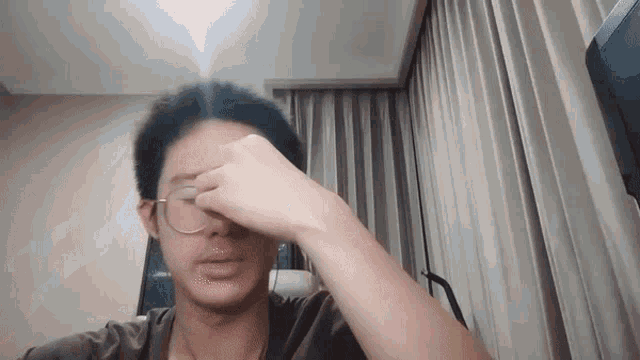 a man wearing glasses is rubbing his nose