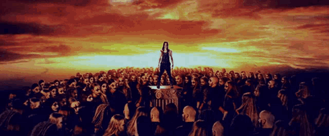 a woman stands in front of a crowd of zombies at sunset