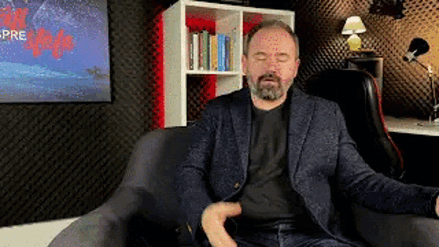 a man in a suit is sitting in a chair with his eyes closed and his hand on his chest .