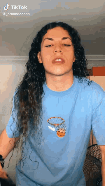a woman with long curly hair wearing a blue shirt with a basketball on it .