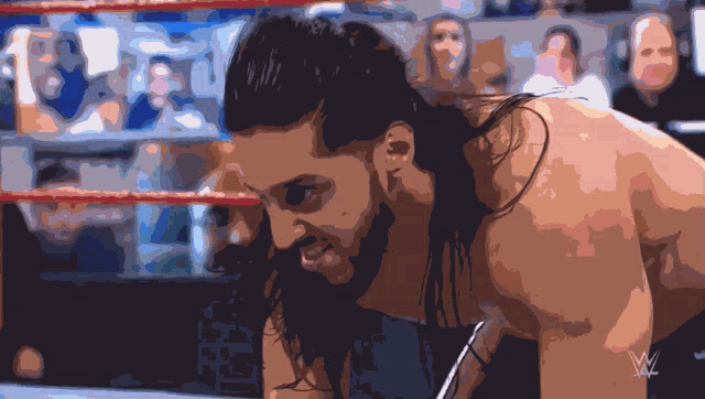 a man with long hair is in a wrestling ring with the letters w on his chest