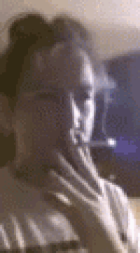 a man is smoking a cigarette in a dark room while holding his hand to his chin .
