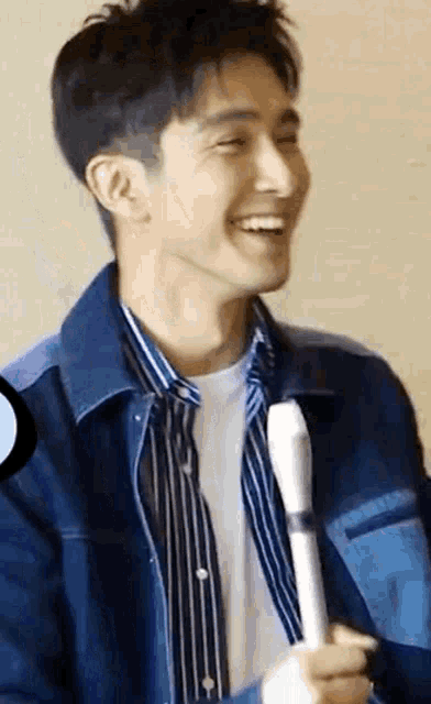 a young man in a denim jacket is smiling while holding a pen .