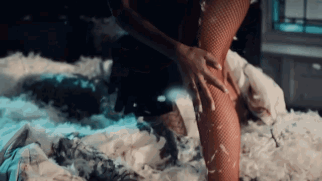 a woman in fishnet stockings is kneeling on a bed covered in feathers and foam .