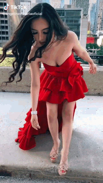 a woman in a red strapless dress is standing on a sidewalk .