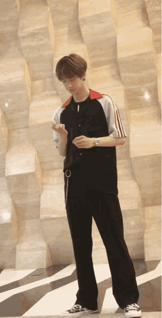 a young man wearing a black shirt and black pants stands in front of a wall